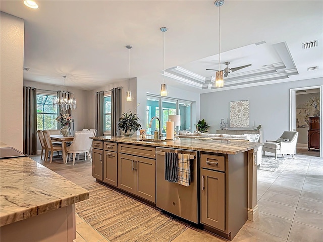 kitchen featuring light stone countertops, ceiling fan with notable chandelier, a raised ceiling, pendant lighting, and an island with sink