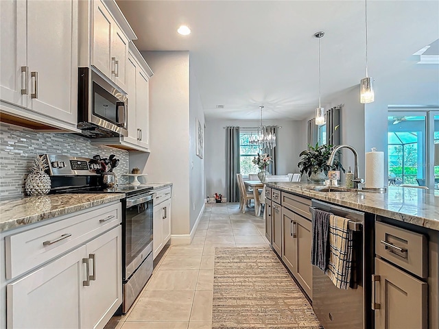 kitchen with pendant lighting, light stone counters, white cabinetry, and appliances with stainless steel finishes