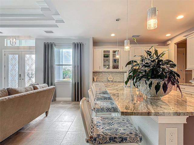 kitchen with a kitchen breakfast bar, light stone countertops, french doors, and hanging light fixtures