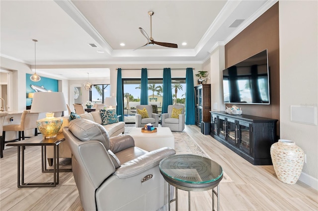 living room featuring a tray ceiling, light hardwood / wood-style flooring, ceiling fan with notable chandelier, and ornamental molding