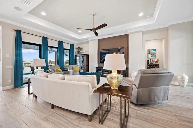 living room with a raised ceiling, ceiling fan, and ornamental molding