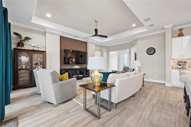 living room featuring a tray ceiling, ceiling fan, and crown molding