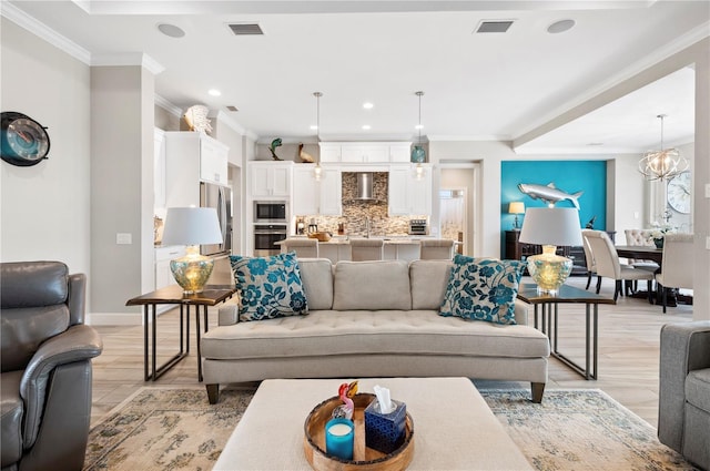 living room with ornamental molding, light hardwood / wood-style floors, a notable chandelier, and sink