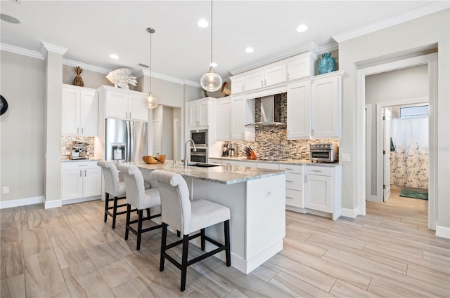 kitchen featuring light stone countertops, wall chimney range hood, pendant lighting, a center island with sink, and white cabinetry