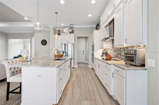 kitchen featuring a center island with sink, decorative light fixtures, white cabinetry, and wall chimney range hood