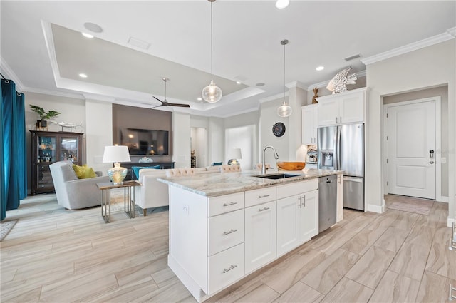 kitchen featuring a center island with sink, a raised ceiling, sink, appliances with stainless steel finishes, and white cabinetry