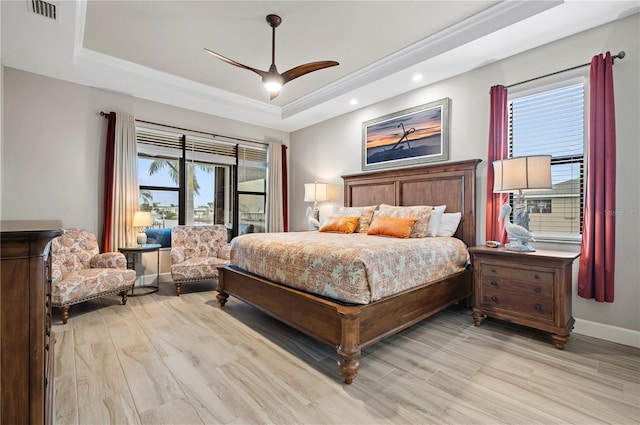 bedroom featuring multiple windows, a tray ceiling, light hardwood / wood-style flooring, and ceiling fan