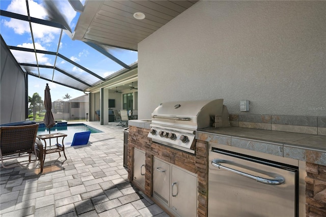 view of patio / terrace with ceiling fan, a grill, exterior kitchen, and glass enclosure