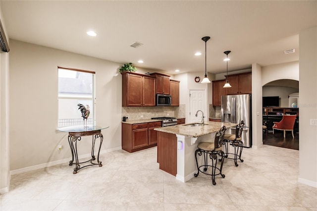 kitchen featuring a kitchen breakfast bar, stainless steel appliances, a kitchen island with sink, sink, and pendant lighting