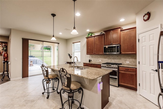 kitchen with sink, hanging light fixtures, an island with sink, light stone counters, and stainless steel appliances