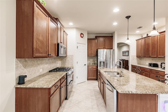 kitchen featuring a center island with sink, sink, decorative light fixtures, light stone counters, and stainless steel appliances