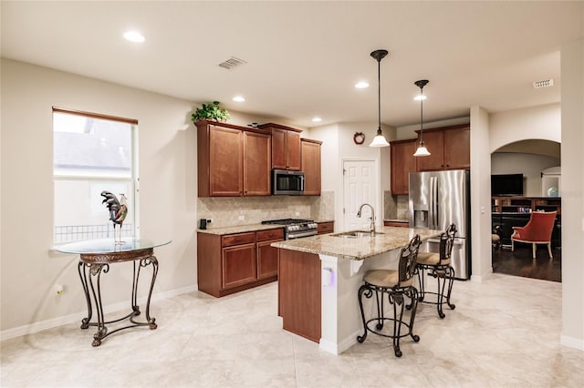 kitchen with pendant lighting, a center island with sink, sink, a kitchen bar, and stainless steel appliances