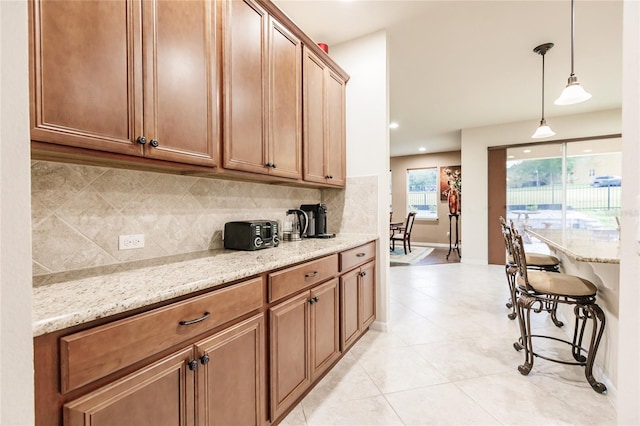 kitchen with tasteful backsplash, light stone counters, light tile patterned floors, and decorative light fixtures