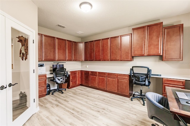 office with light hardwood / wood-style flooring, built in desk, and a textured ceiling