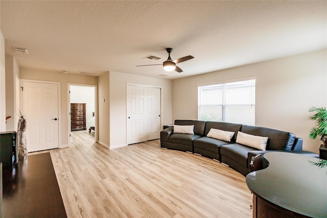 living room featuring ceiling fan, light hardwood / wood-style flooring, and a textured ceiling