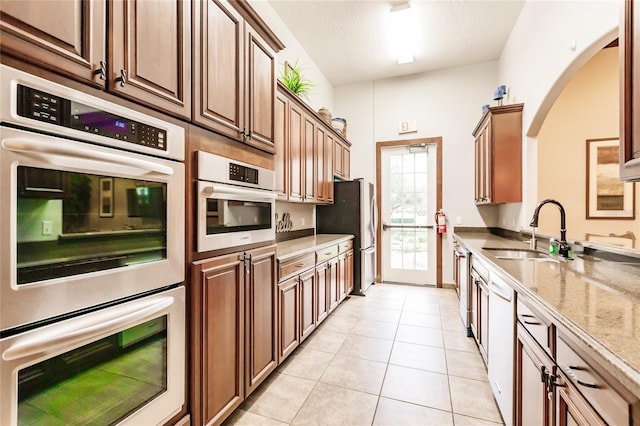 kitchen featuring appliances with stainless steel finishes, light tile patterned floors, light stone counters, and sink