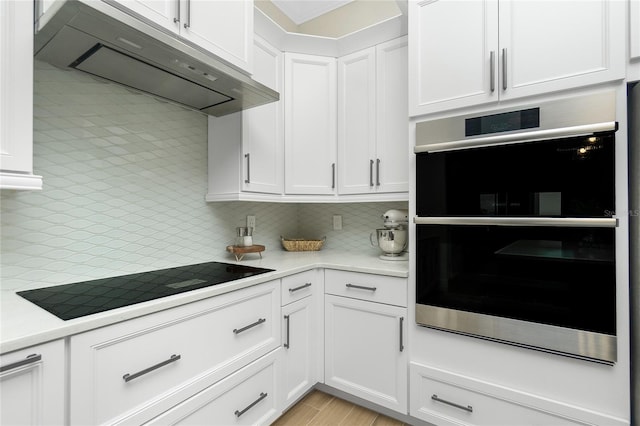 kitchen with double oven, tasteful backsplash, white cabinets, wall chimney range hood, and black electric cooktop