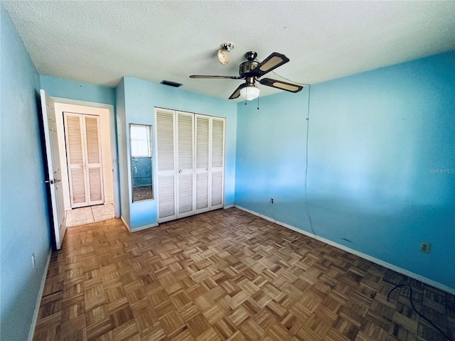 unfurnished bedroom with dark parquet floors, ceiling fan, and a textured ceiling