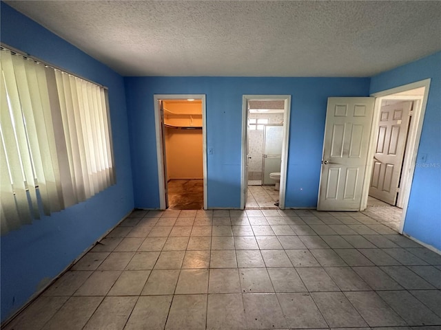 unfurnished bedroom with a spacious closet, a closet, ensuite bathroom, and a textured ceiling