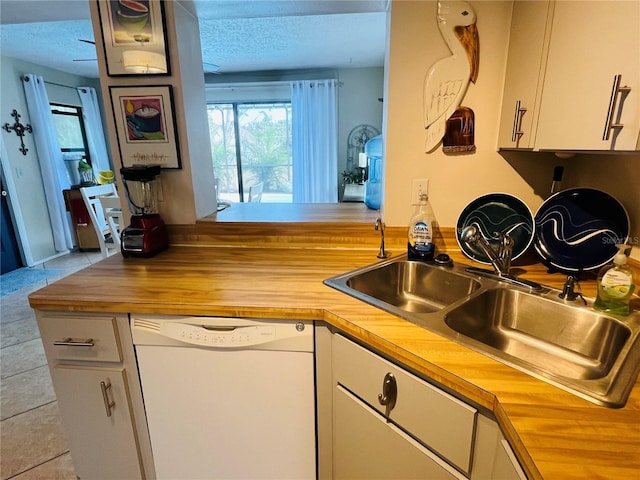 kitchen with wooden counters, sink, white dishwasher, white cabinetry, and light tile patterned floors