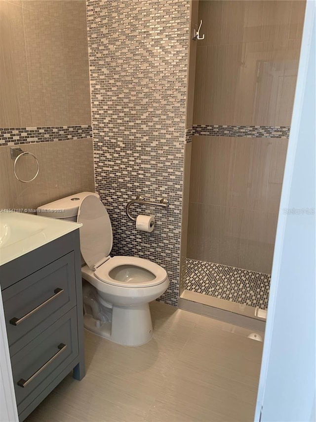 bathroom featuring a shower, vanity, tile walls, and toilet