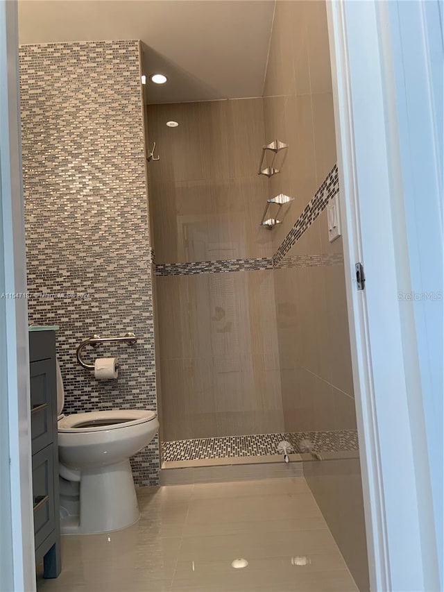 bathroom with a tile shower, tile patterned flooring, toilet, vanity, and tile walls