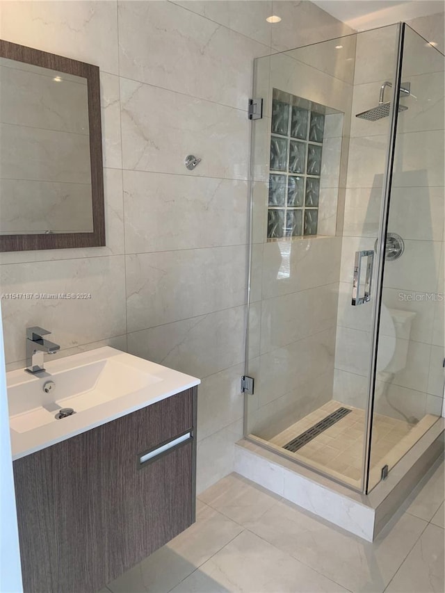 bathroom with tile patterned flooring, vanity, an enclosed shower, and tile walls