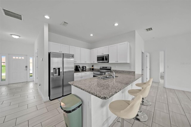 kitchen with sink, a breakfast bar area, dark stone countertops, kitchen peninsula, and stainless steel appliances