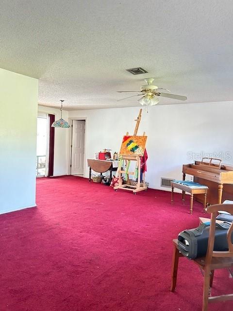sitting room with a textured ceiling, visible vents, a ceiling fan, and carpet