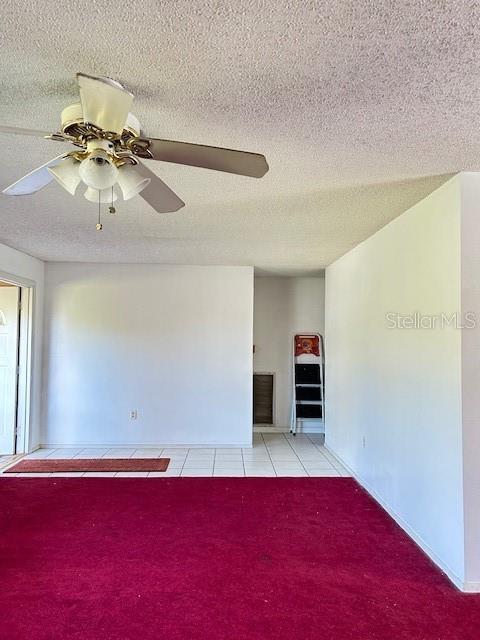 unfurnished living room featuring light carpet, a textured ceiling, a ceiling fan, and light tile patterned flooring