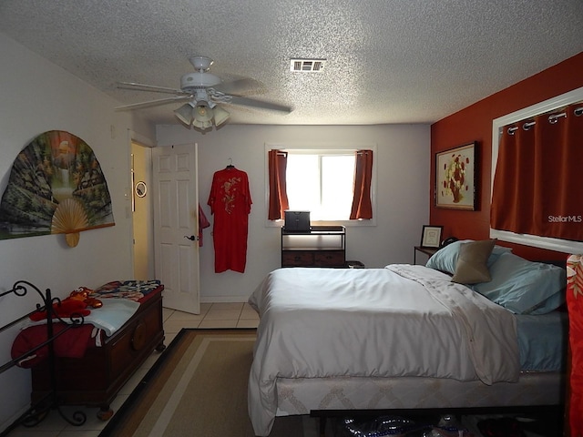 bedroom featuring a textured ceiling, light tile patterned floors, a ceiling fan, and visible vents