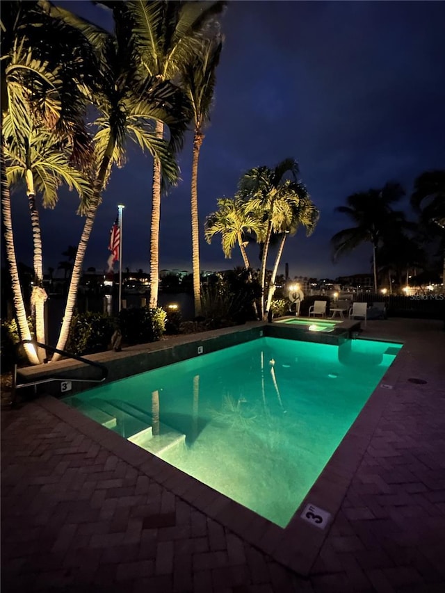 pool at night featuring an in ground hot tub