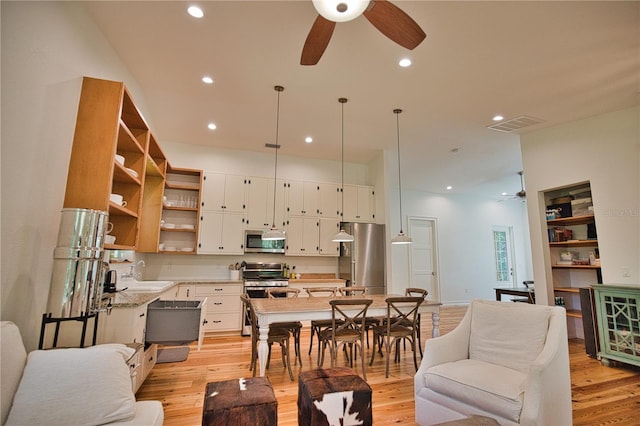 living room featuring built in shelves, light hardwood / wood-style flooring, ceiling fan, and sink