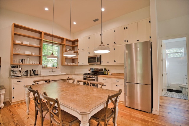 kitchen with pendant lighting, white cabinets, stainless steel appliances, and light wood-type flooring