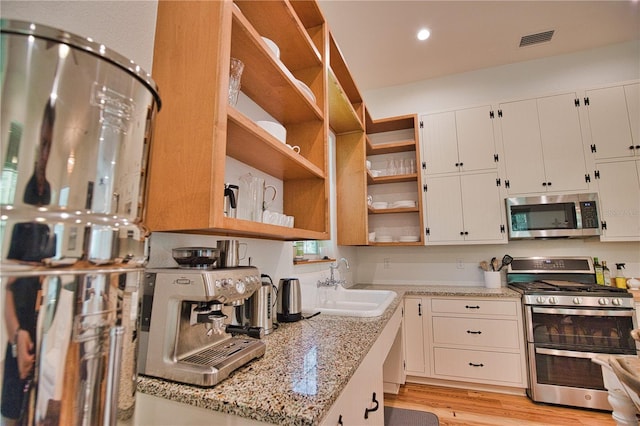 kitchen with light stone countertops, appliances with stainless steel finishes, sink, light hardwood / wood-style floors, and white cabinetry