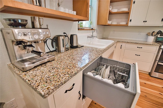 kitchen with light hardwood / wood-style floors, light stone counters, sink, and stainless steel range