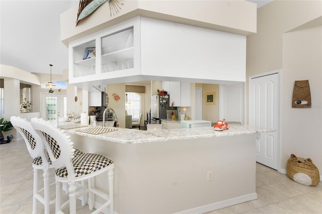 kitchen with kitchen peninsula, stainless steel fridge, white cabinets, a high ceiling, and hanging light fixtures