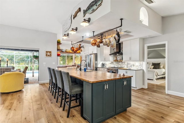 kitchen featuring wood counters, sink, white cabinetry, a center island with sink, and stainless steel appliances