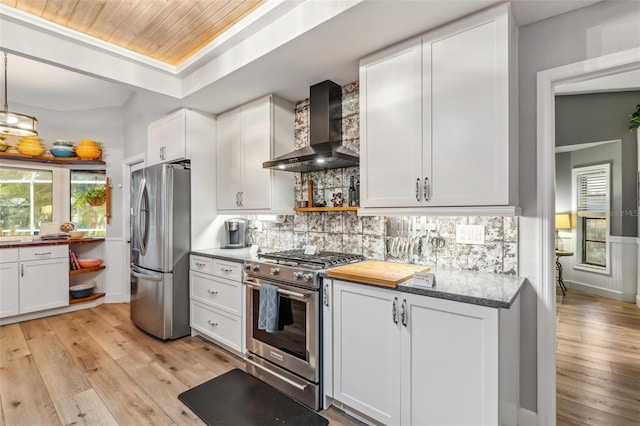 kitchen with decorative backsplash, appliances with stainless steel finishes, white cabinets, and wall chimney exhaust hood