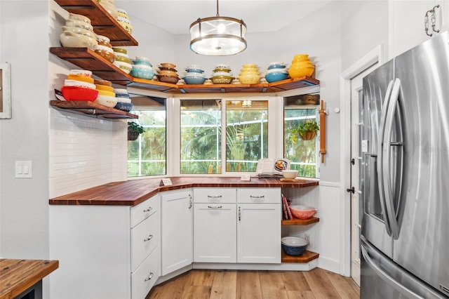 kitchen with white cabinetry, stainless steel fridge, butcher block counters, and decorative light fixtures