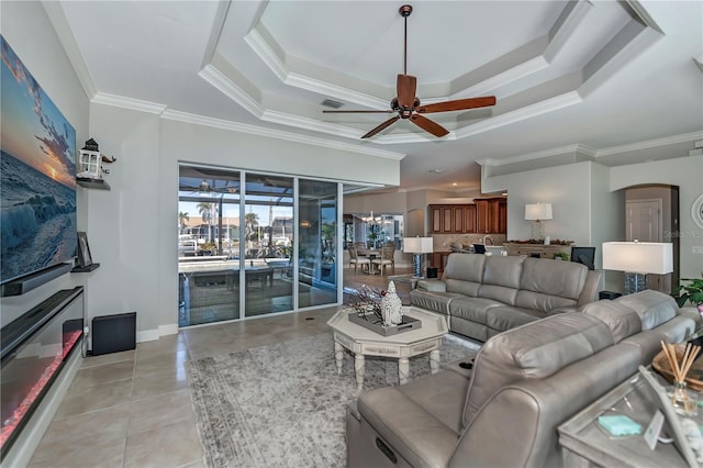 tiled living room featuring ceiling fan, a tray ceiling, and crown molding