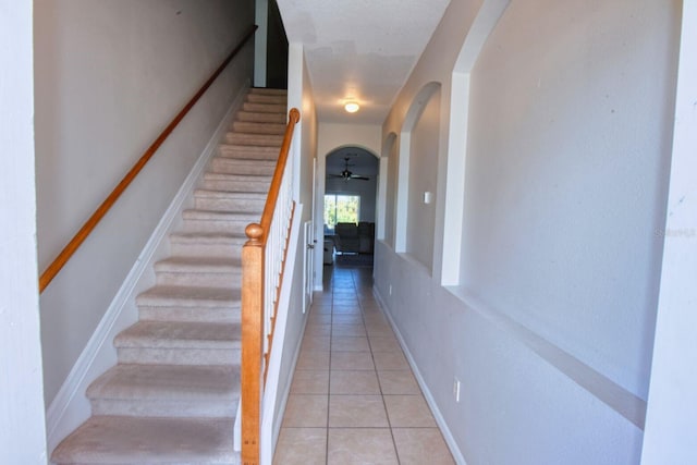 stairs featuring tile patterned floors, baseboards, arched walkways, and ceiling fan