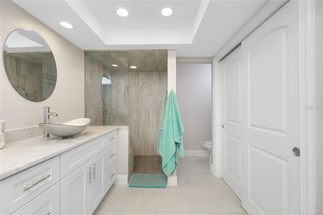 bathroom featuring a tile shower, tile patterned flooring, vanity, a tray ceiling, and toilet