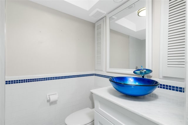 bathroom featuring vanity, tile walls, and toilet