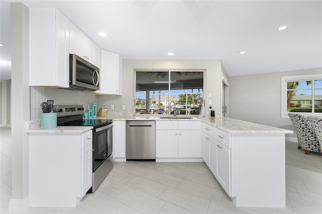 kitchen featuring sink, white cabinets, kitchen peninsula, stainless steel appliances, and light stone countertops