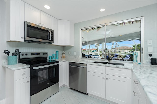 kitchen with appliances with stainless steel finishes, white cabinetry, sink, light tile patterned floors, and light stone countertops