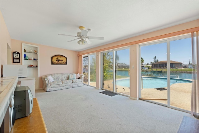 unfurnished living room featuring light colored carpet, ceiling fan, a water view, and built in features