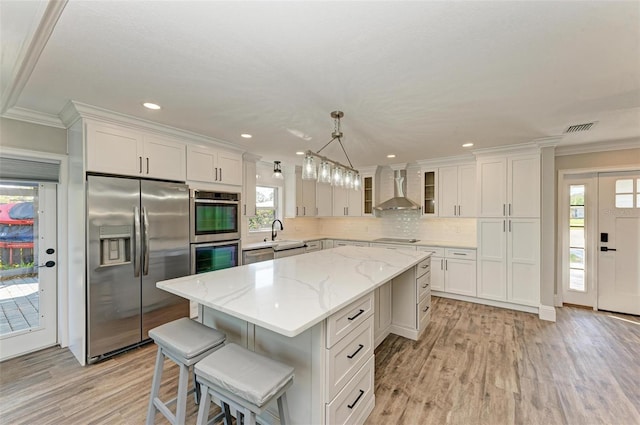 kitchen featuring stainless steel appliances, white cabinets, wall chimney range hood, and a center island