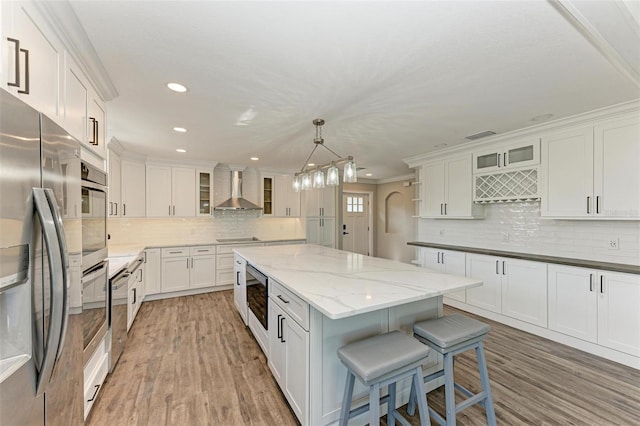 kitchen with appliances with stainless steel finishes, wall chimney range hood, pendant lighting, and white cabinetry