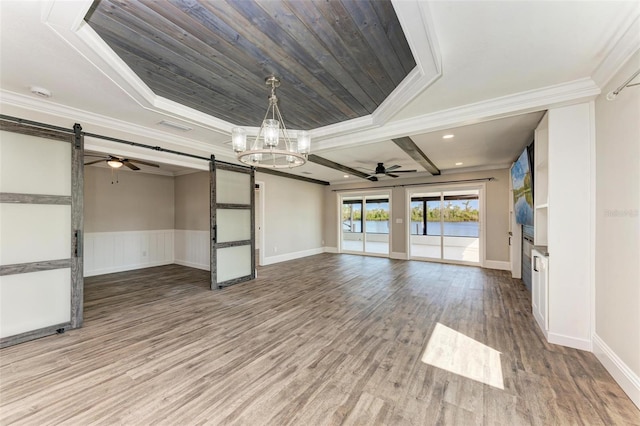 unfurnished living room with ceiling fan with notable chandelier, hardwood / wood-style flooring, ornamental molding, and a barn door